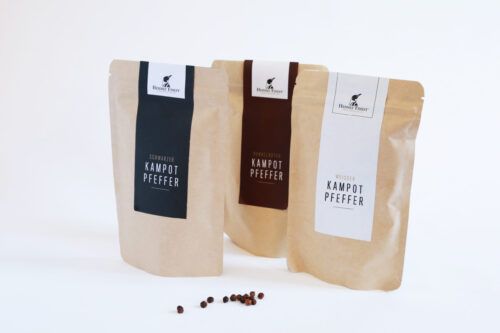 Drei Tüten mit Kampot-Pfeffer, jede Tüte zeigt eine unterschiedliche Verpackung und Etikettierung. 