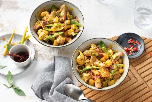 Rezept für Putencurry mit buntem Gemüse in zwei Schüsseln, umgeben von frischen Kräutern und Gewürzen. 