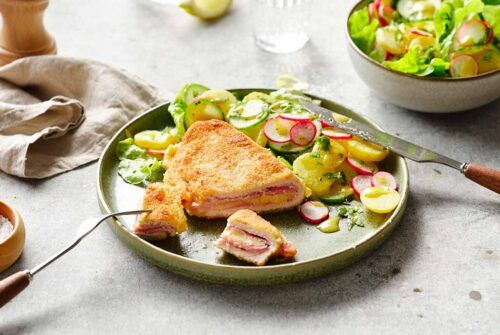 Cordon bleu vom Schwein, knusprig und goldbraun, neben einem frischen Kartoffel-Gurkensalat auf einem Tisch angerichtet.
